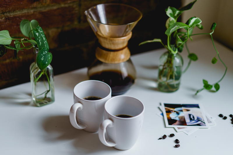 Two coffee mugs and a coffee maker on a white table.