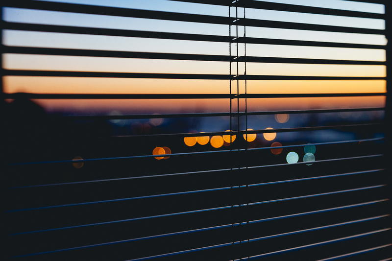 A view of a city from a window with blinds.