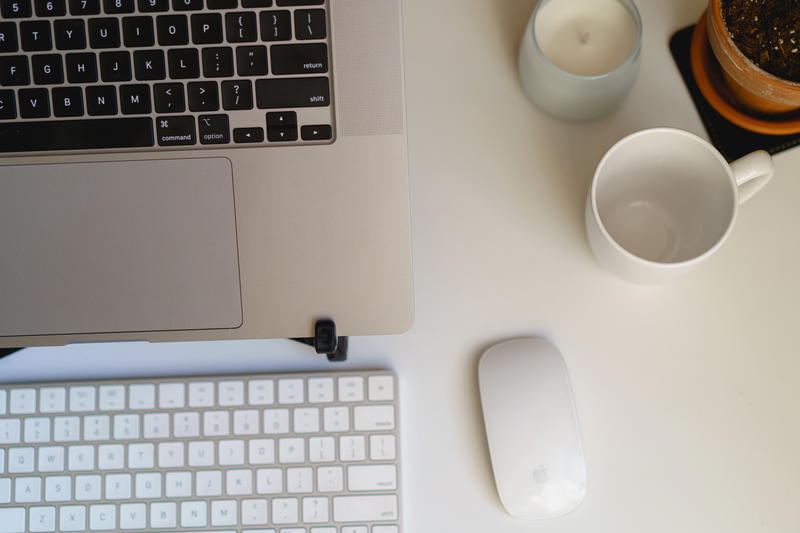 Flat lay view of home office setup with MacBook Pro laptop, wireless keyboard, wireless mouse, candle, mug and plant on a slim white desk surface