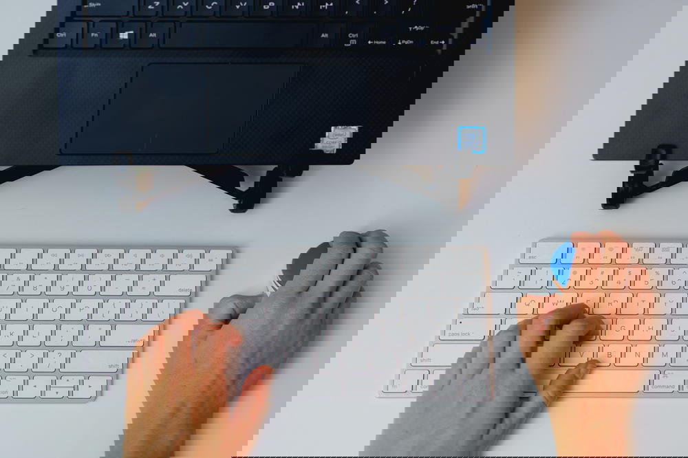 Woman using a small wireless mouse with an apple magic keyboard and laptop on a laptop stand in a home office setup
