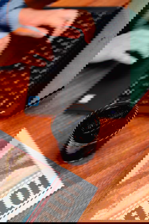 Delicate glass full of cold brew iced coffee next to a black laptop with a girl typing on the keyboard