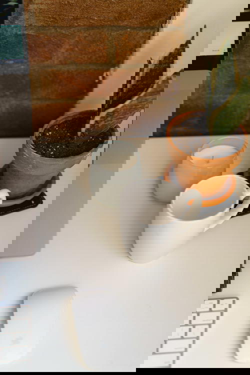 White home office desk with white mug, small candle, potted plant and white wireless mouse against an exposed brick wall