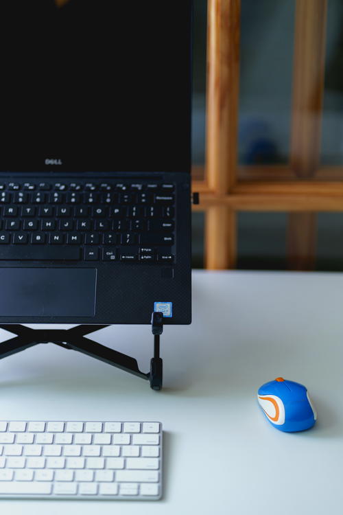 Mini logitech external mouse used with a laptop in a laptop stand and external keyboard in a home office setup