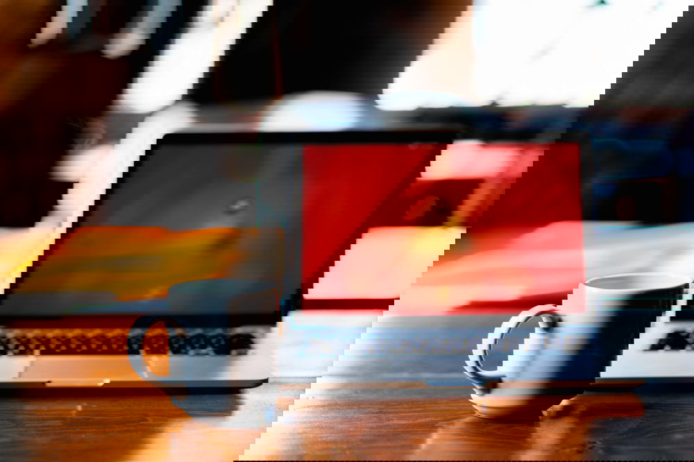 Big white coffee mug next to a MacBook Pro on a wooden table desk in a coworking space