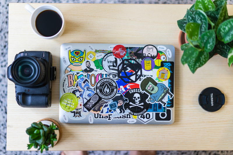 Flat lay shot on a light wooden coffee table of a silver laptop covered in stickers with a succulent, plant and cup of coffee